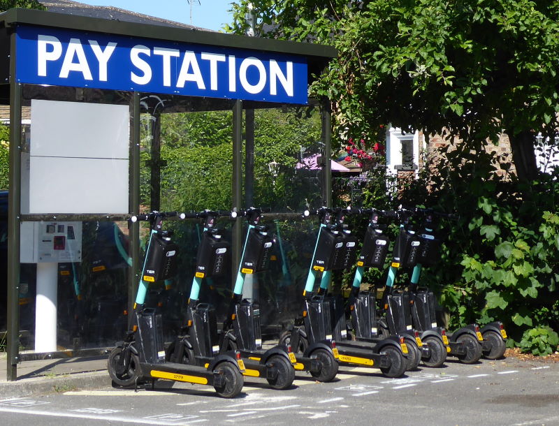 A row of e-scooters parked up at a docking station in a car park