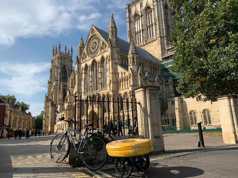 A bike towing a trailer in front of York Minster with a stack of bright yellow hula hoops on it.