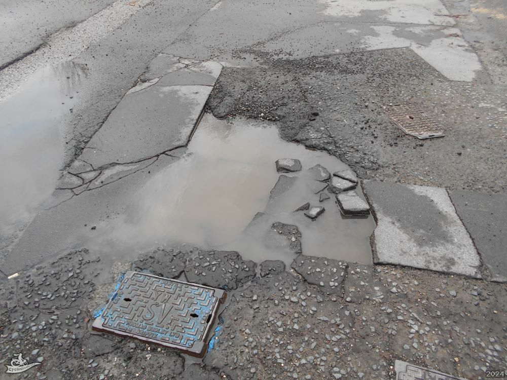 A broken manhole cover half covered by a puddle 