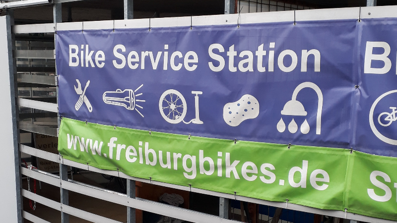 A banner for a Bike Service Station with symbols indicating facilities for tools, lights, bike pumps, bike cleaning, showers, and parking 