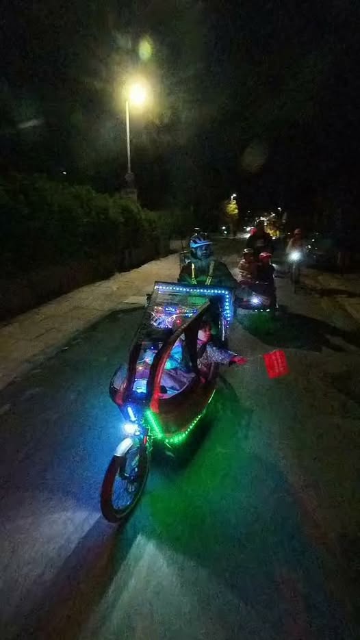 Brightly illuminated cargo bikes participating in a nighttime glow ride, adorned with decorative lights and riding on a quiet street.