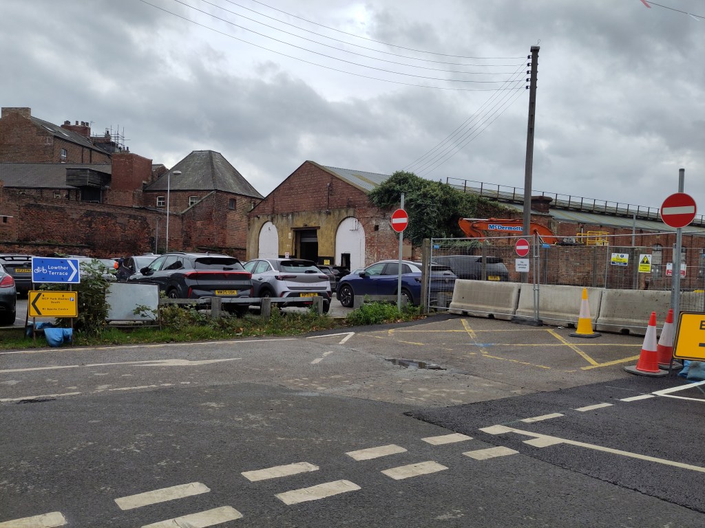 A view of a street with parked cars, barriers, and traffic signs indicating restricted access to a construction area in York.